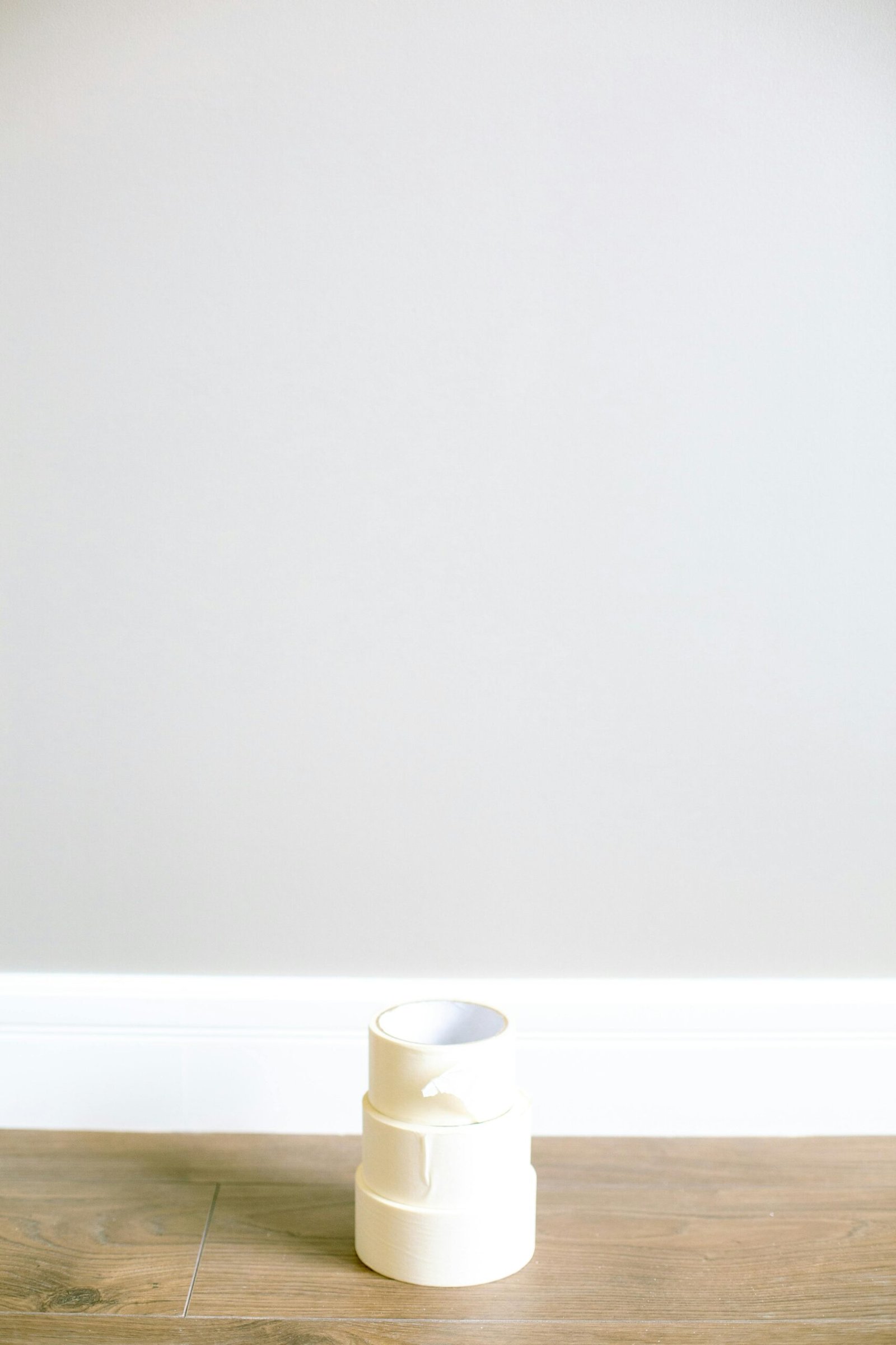 A stack of masking tape rolls on a wooden floor against a neutral painted wall, perfect for renovation projects.